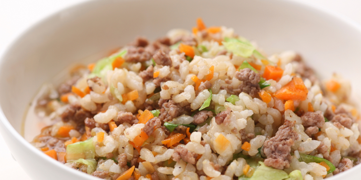 A white bowl filled with rice , meat and vegetables.