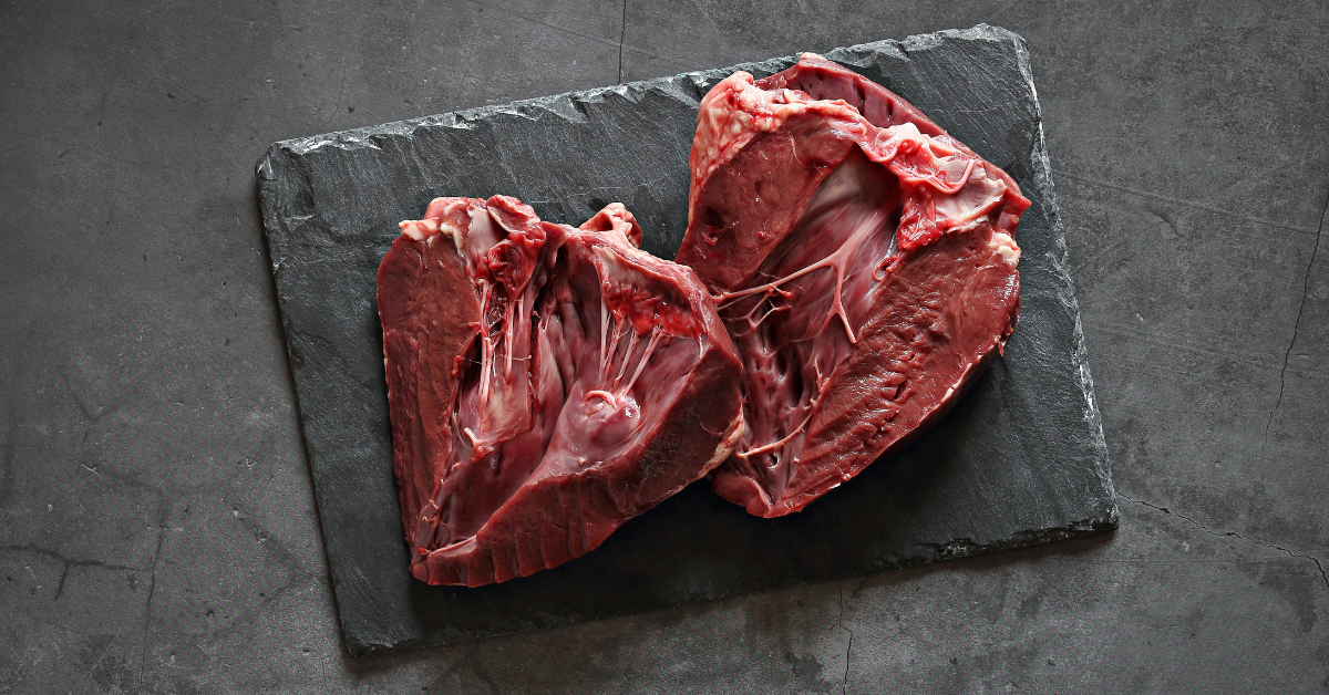 two raw beef hearts are cut in half on a slate cutting board .