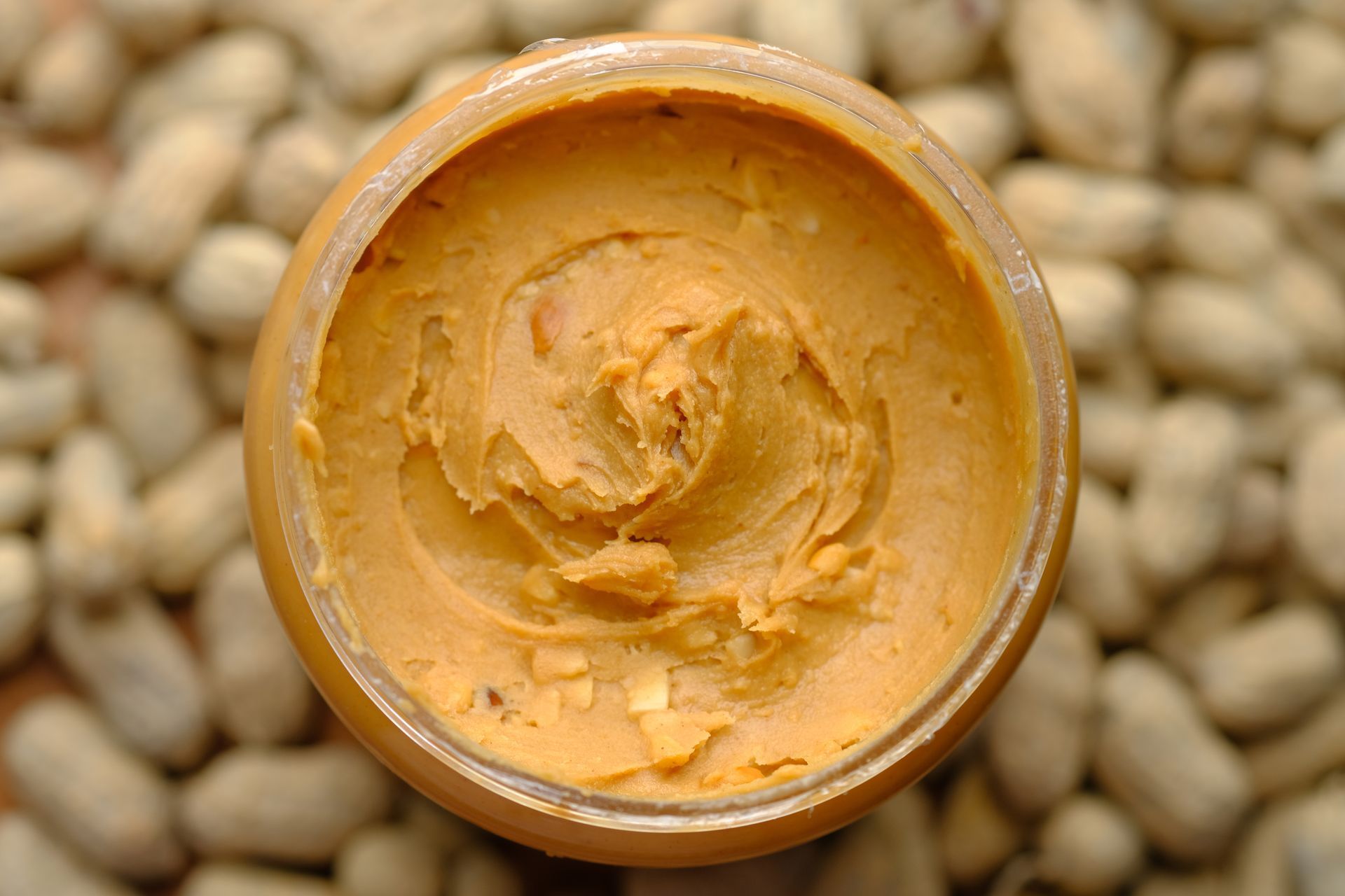 a jar of peanut butter is sitting on top of a pile of peanuts .