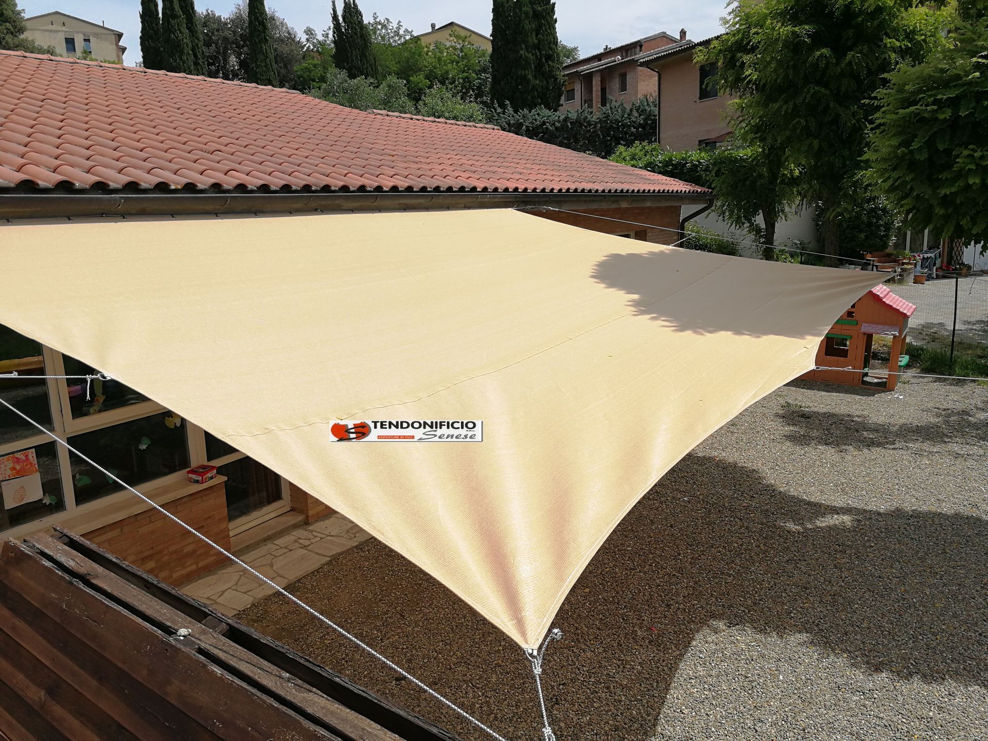 una grande vela ombreggiante pende da un recinto davanti a una casa.