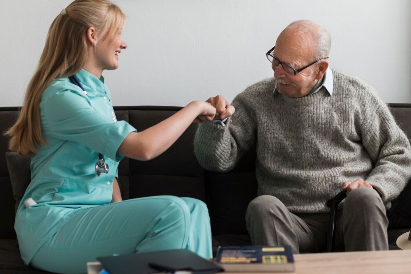 A nurse is giving an elderly man a high five while sitting on a couch.