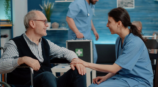 A nurse is holding the hand of an elderly man in a wheelchair.