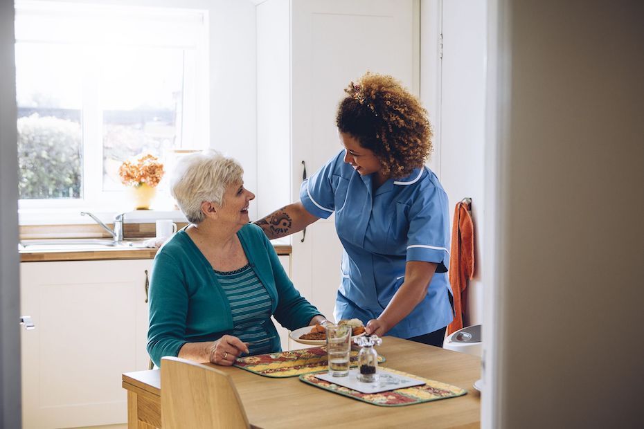 A nurse is helping an elderly woman sit at a table.
