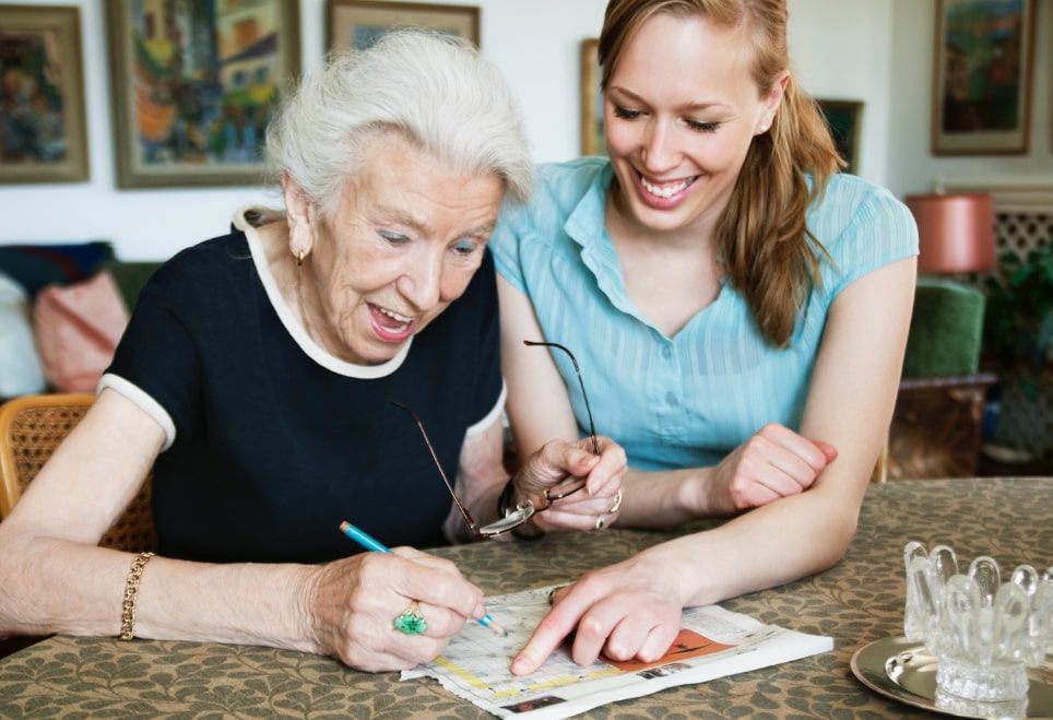 Woman helping elderly person with a crossword puzzle.