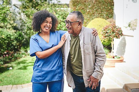 A nurse is standing next to an older man in a garden.