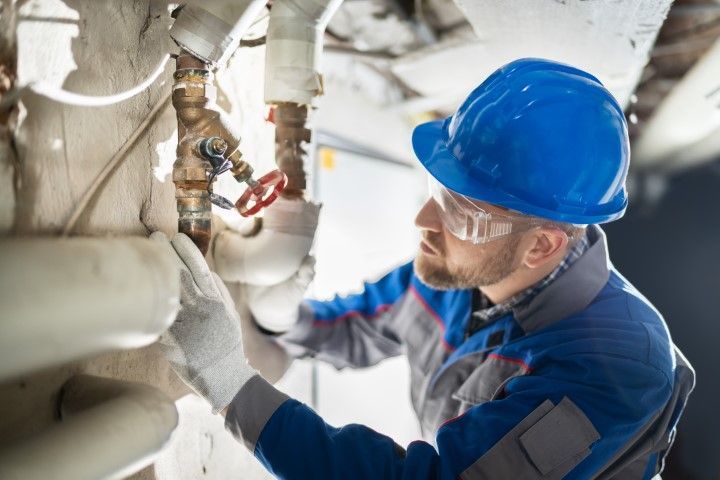 Worker in blue hard hat inspecting pipes and valves in a bright industrial facility