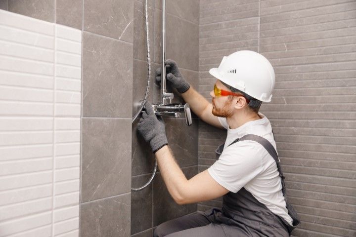 Technician wearing hard hat and gloves installing electrical wiring on a tiled wall