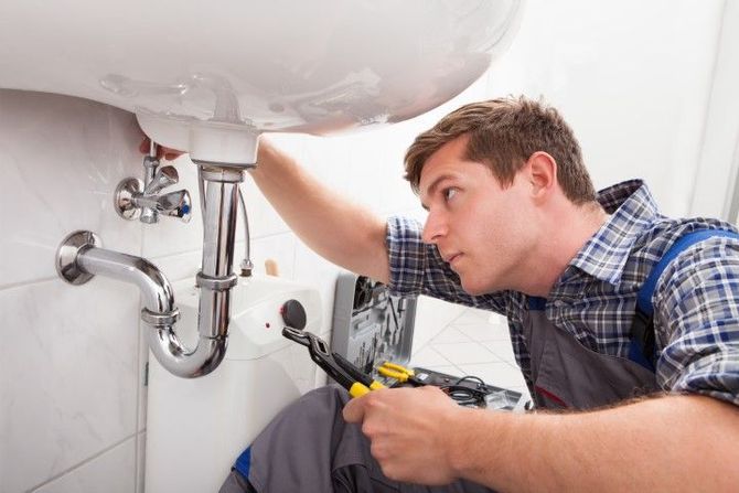 Plumber repairing sink pipes under a bathroom vanity with a wrench