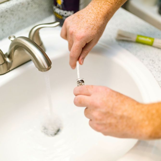 Hands brushing teeth under a running bathroom faucet at a sink