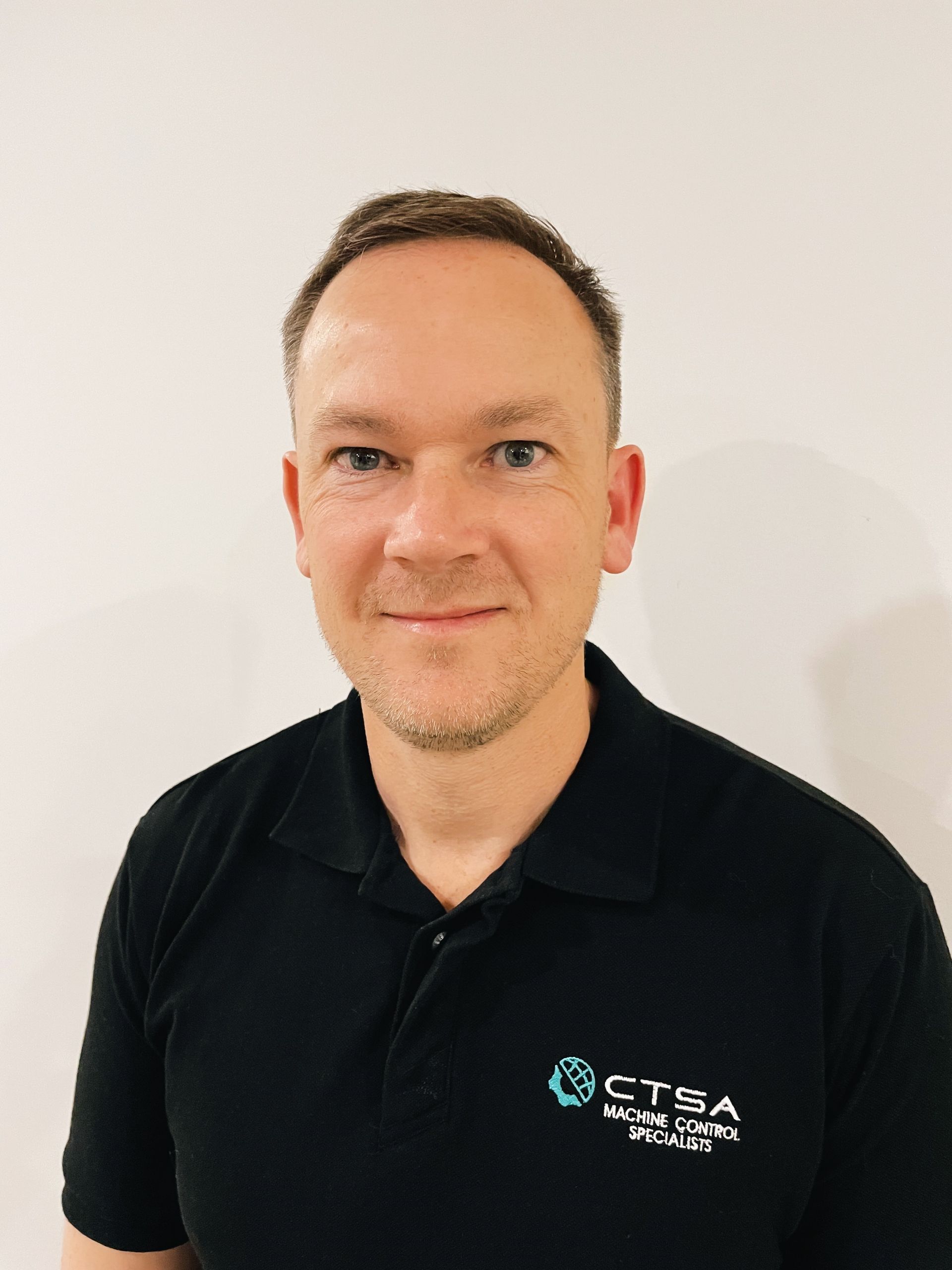 Man in black polo shirt smiles at camera. CTRA logo on shirt. White background.