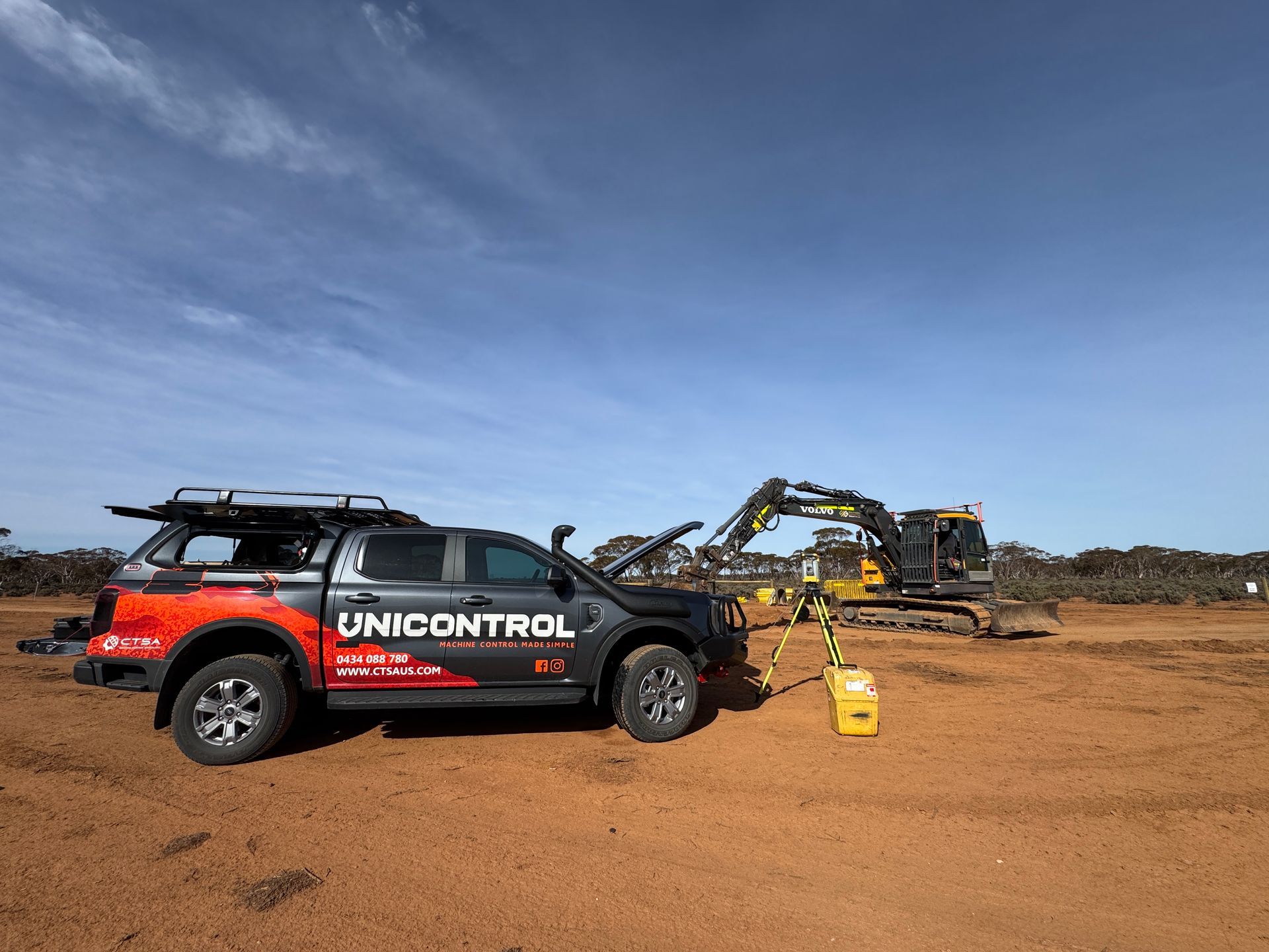 Yellow backhoe at construction site, worker walks by, blue sky.