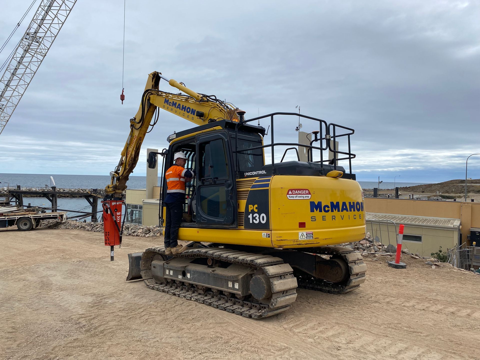 Yellow excavator with a person in the cabin on a construction site next to water.