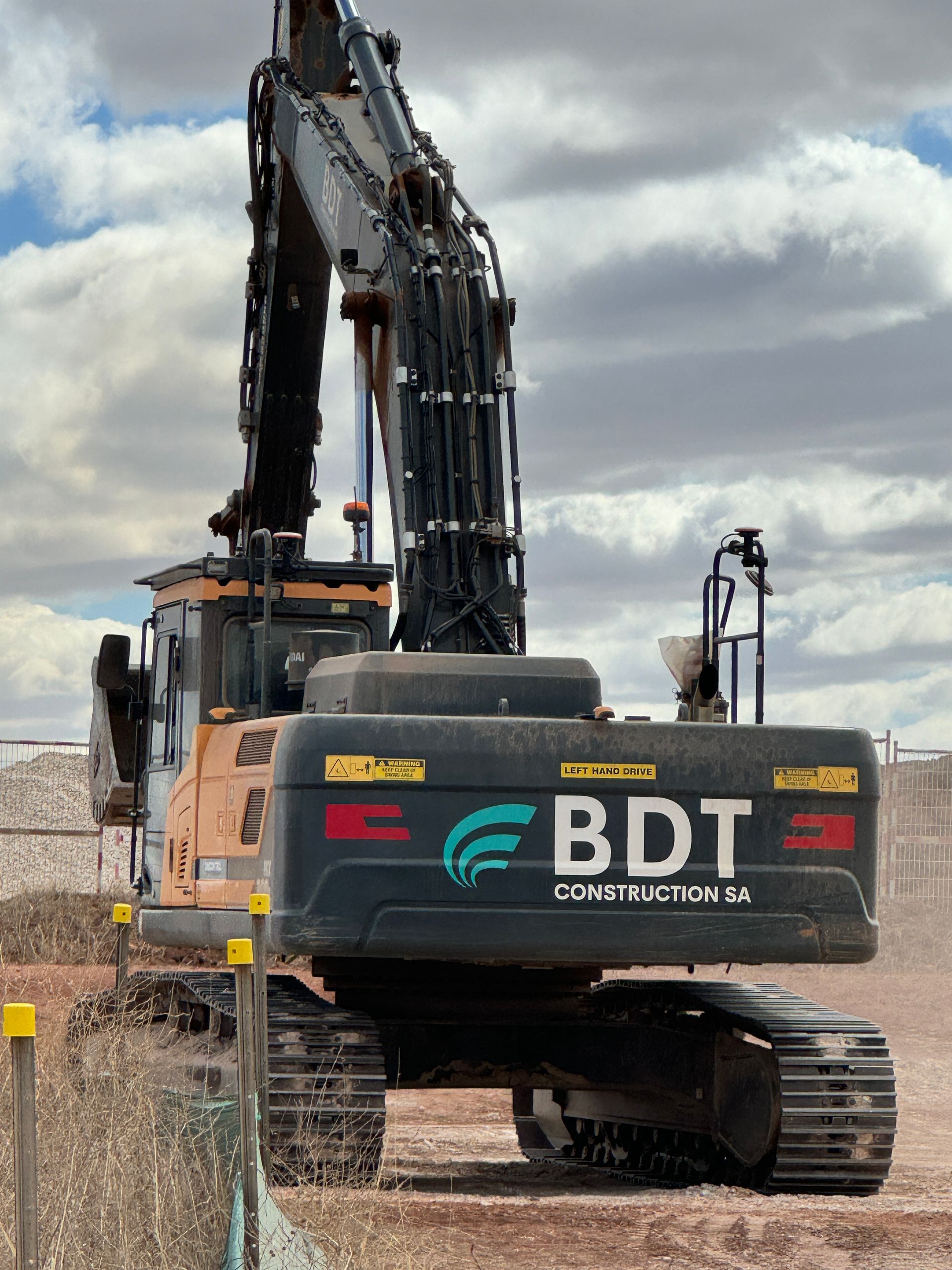 A large construction excavator, black and orange, with the BDT Construction logo.