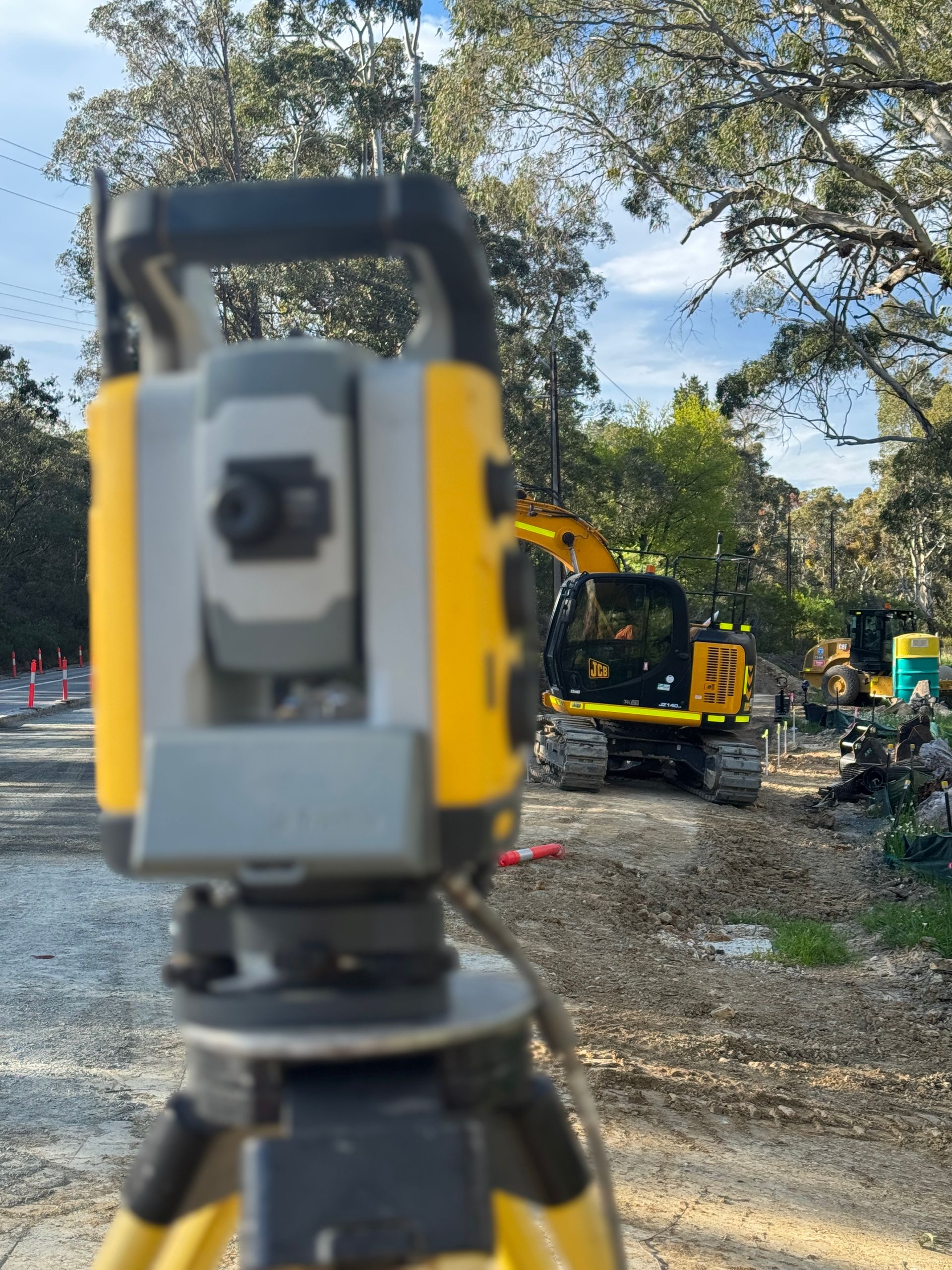 Surveying equipment on a tripod, in front of a construction site with an excavator.