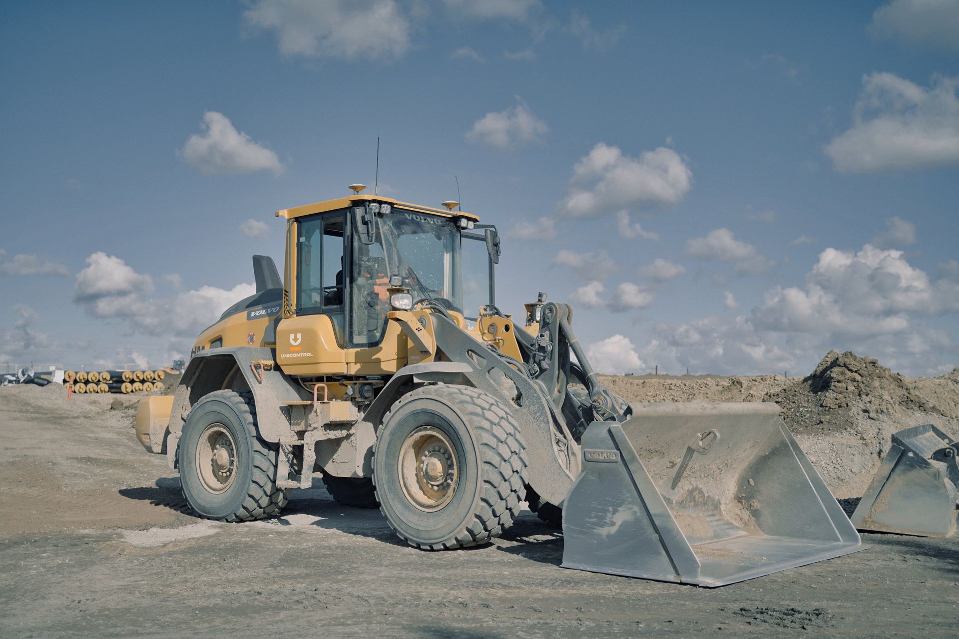 Yellow loader on a construction site with the bucket down, against a blue sky with clouds.