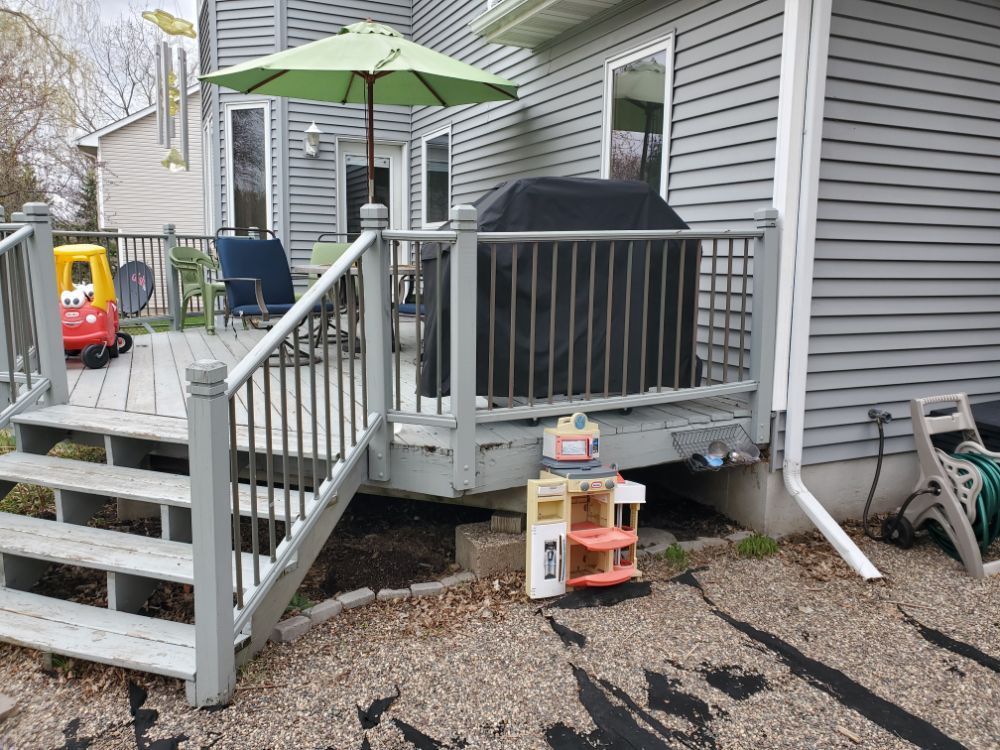 Gray wooden deck with grill, umbrella, and toy kitchen set against a gray house.