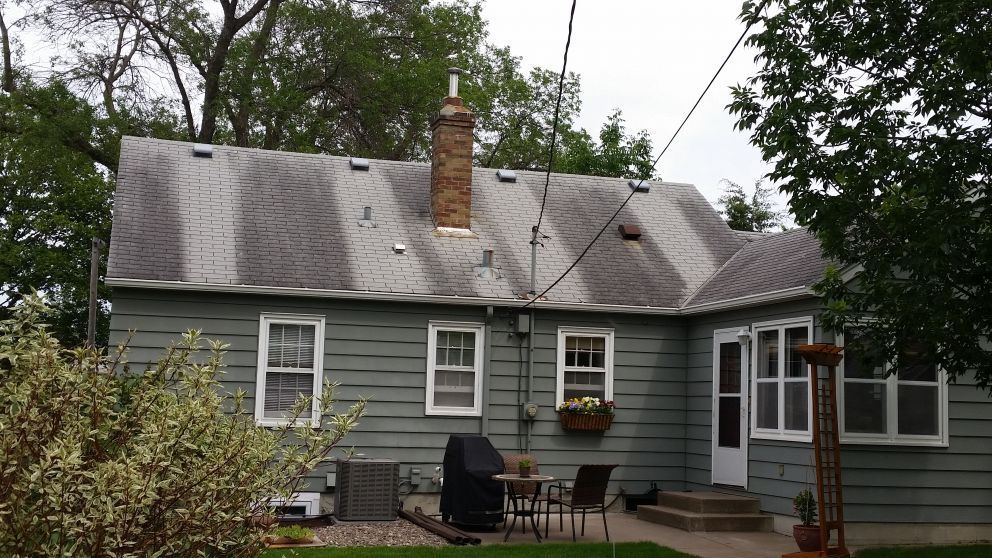Green house with gray roof, chimney, and power lines. There is a small patio table and chairs.