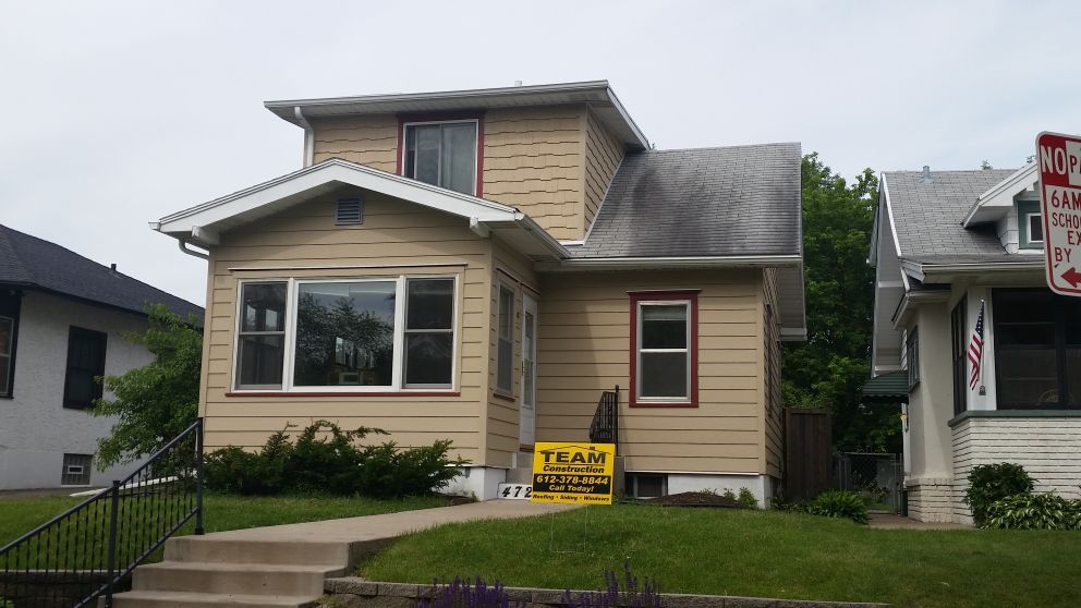 Tan two-story house with green grass and steps leading to the front door. A Team Realty sign is in front.
