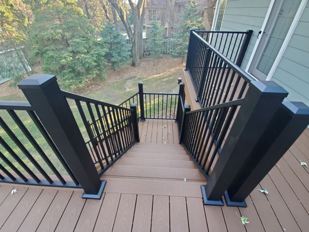 Wooden deck stairs with black railings leading down to a yard with trees.