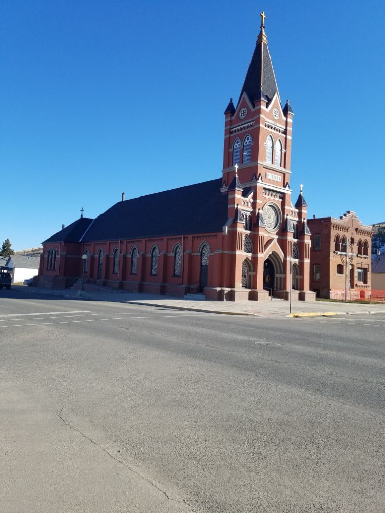 Red brick church with tall spire under a blue sky, on a street.