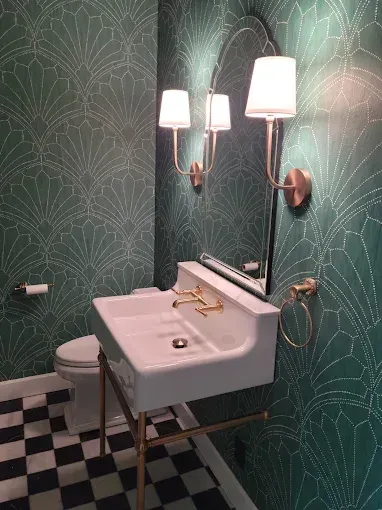 Small bathroom with green patterned wallpaper, white sink, gold fixtures, and black and white checkered floor.