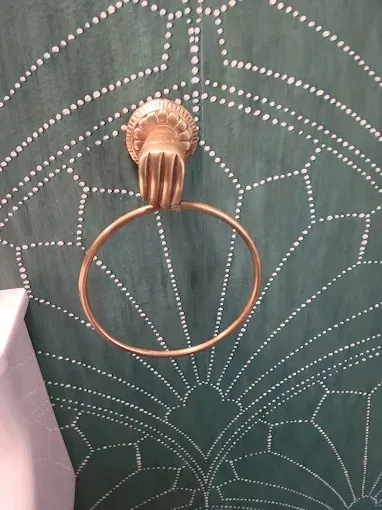 Gold hand-shaped towel ring on teal wall with white dotted design.