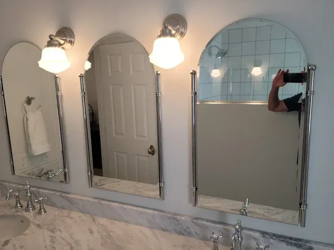 Three arched mirrors above a marble countertop with chrome fixtures and lights in a bathroom.