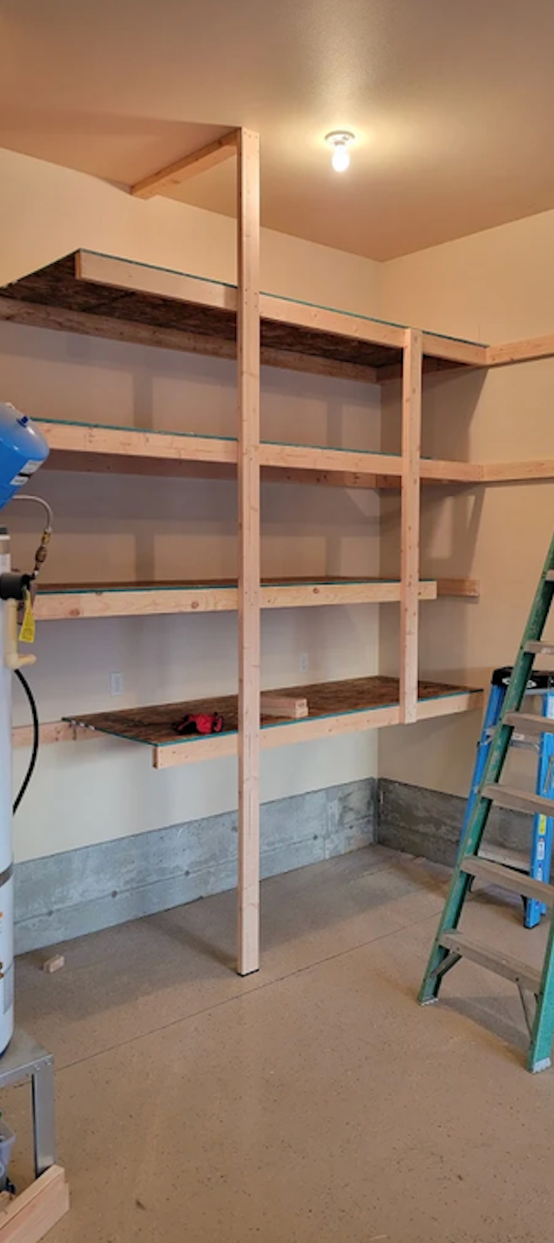 A set of unfinished wooden shelves constructed in a garage with a ladder on the right.