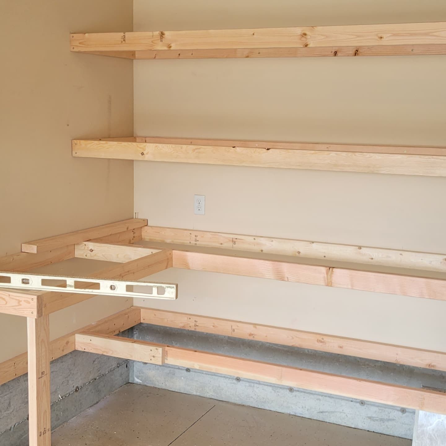 Wooden shelving under construction in a corner, with shelves and framing attached to the wall.