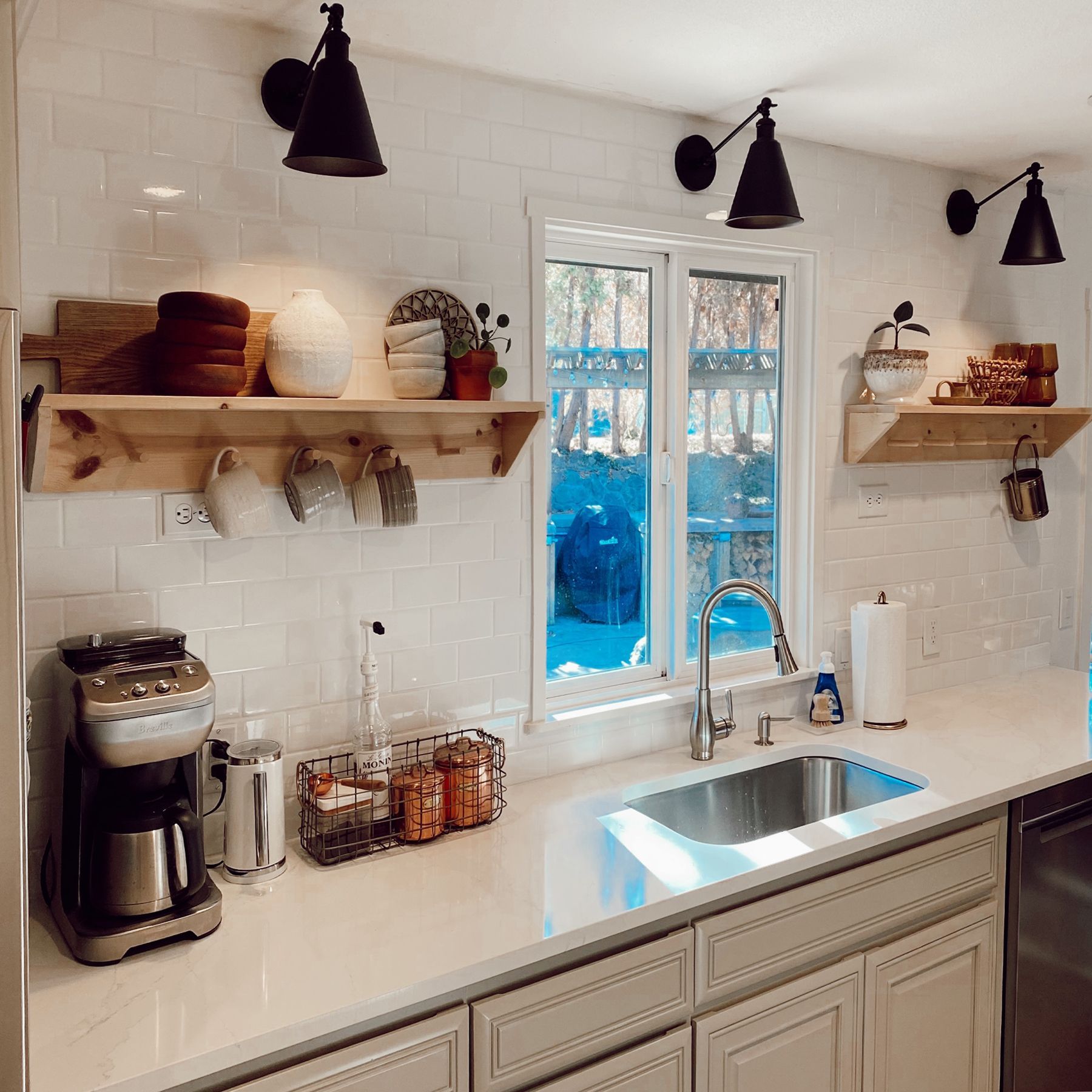 Kitchen with white countertops, shelves with dishes, and black wall-mounted lights.