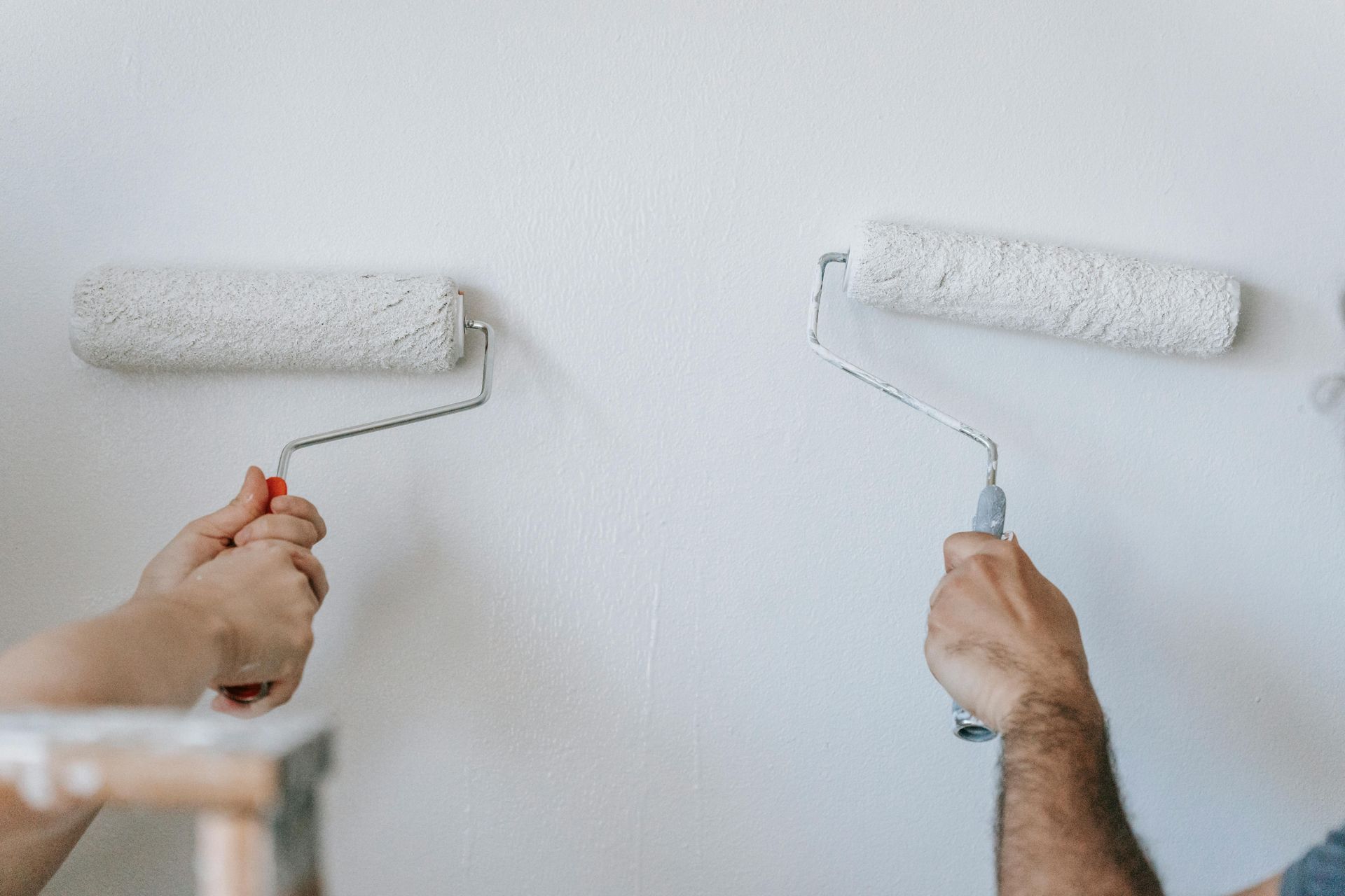Two people painting a white wall with paint rollers.