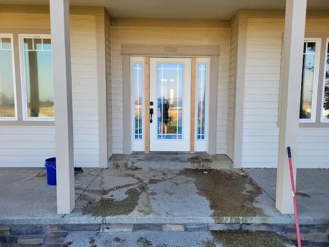 Front porch with wet concrete, entry door with sidelights, and support columns.