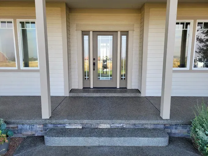 Beige home entryway with steps and a gray textured concrete porch.