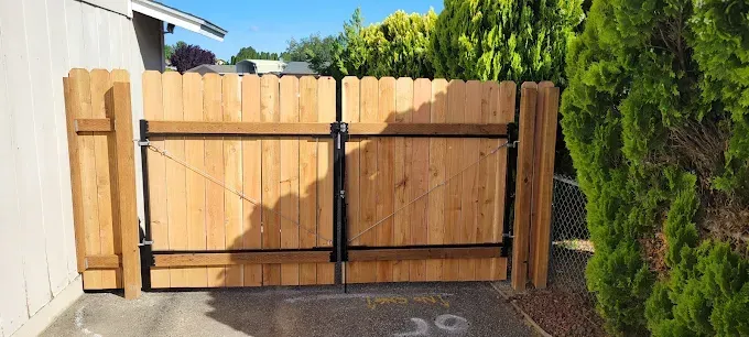 Wooden fence gate, open to the left, with lush green foliage on the right.