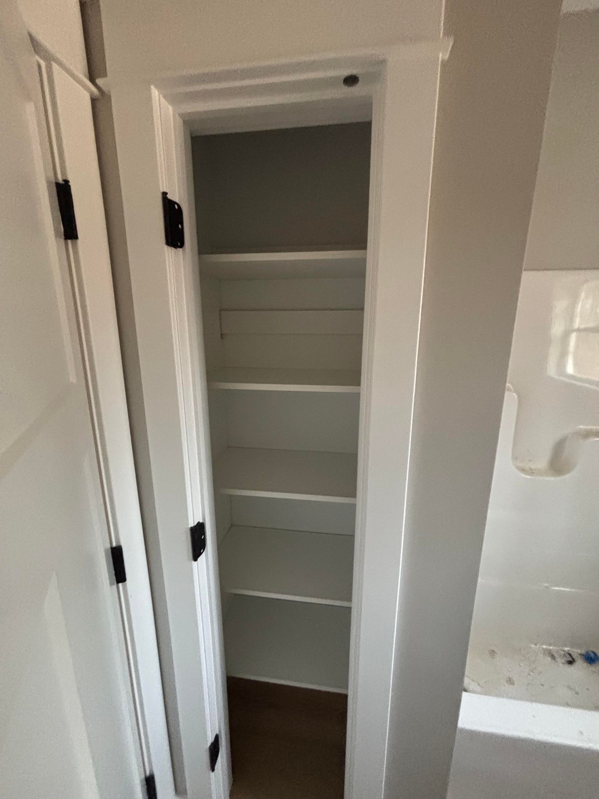 A closet with shelves in a bathroom next to a sink.