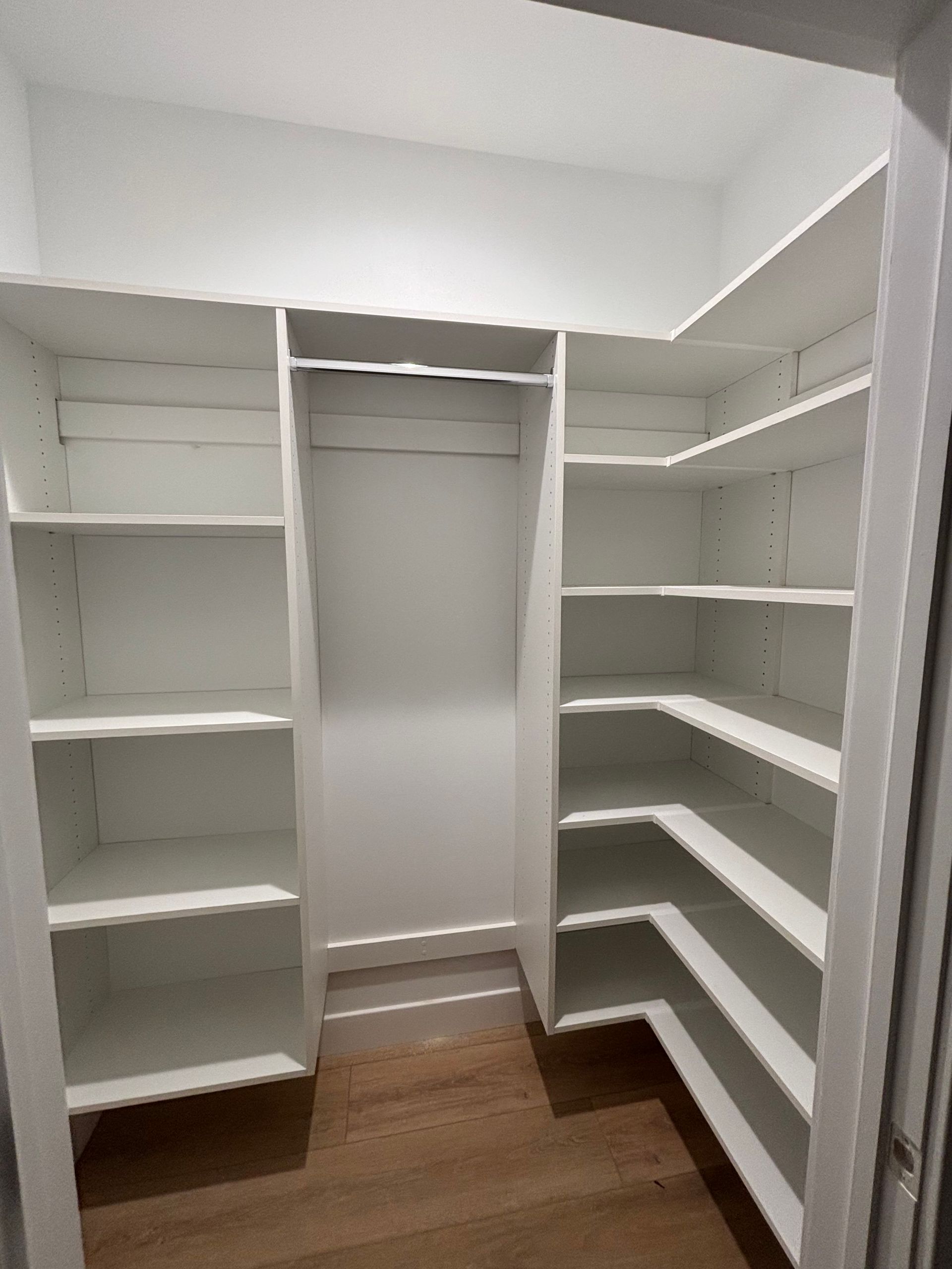 A walk in closet with white shelves and a wooden floor.