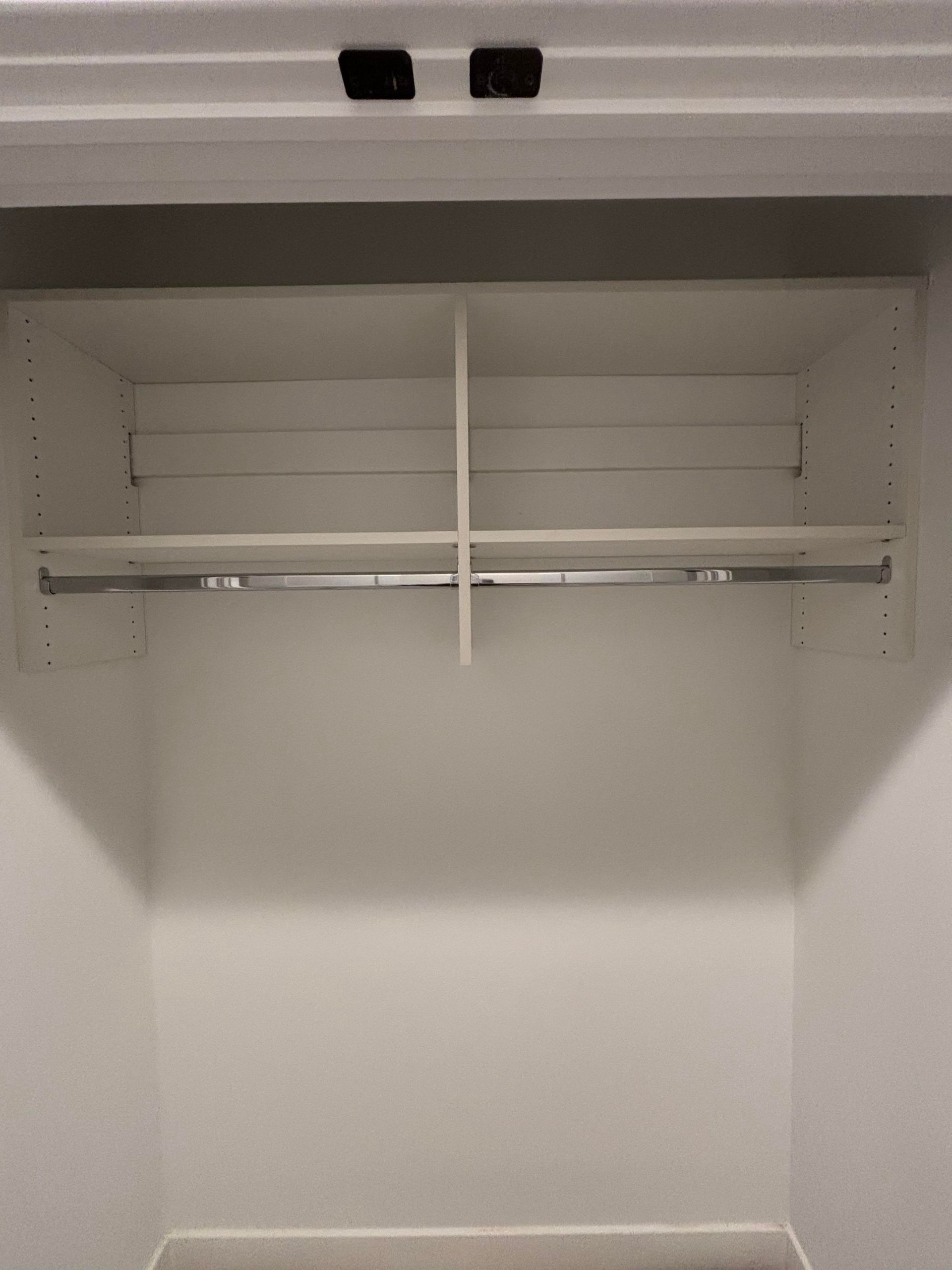 A closet with a shelf and a clothes rack in it.