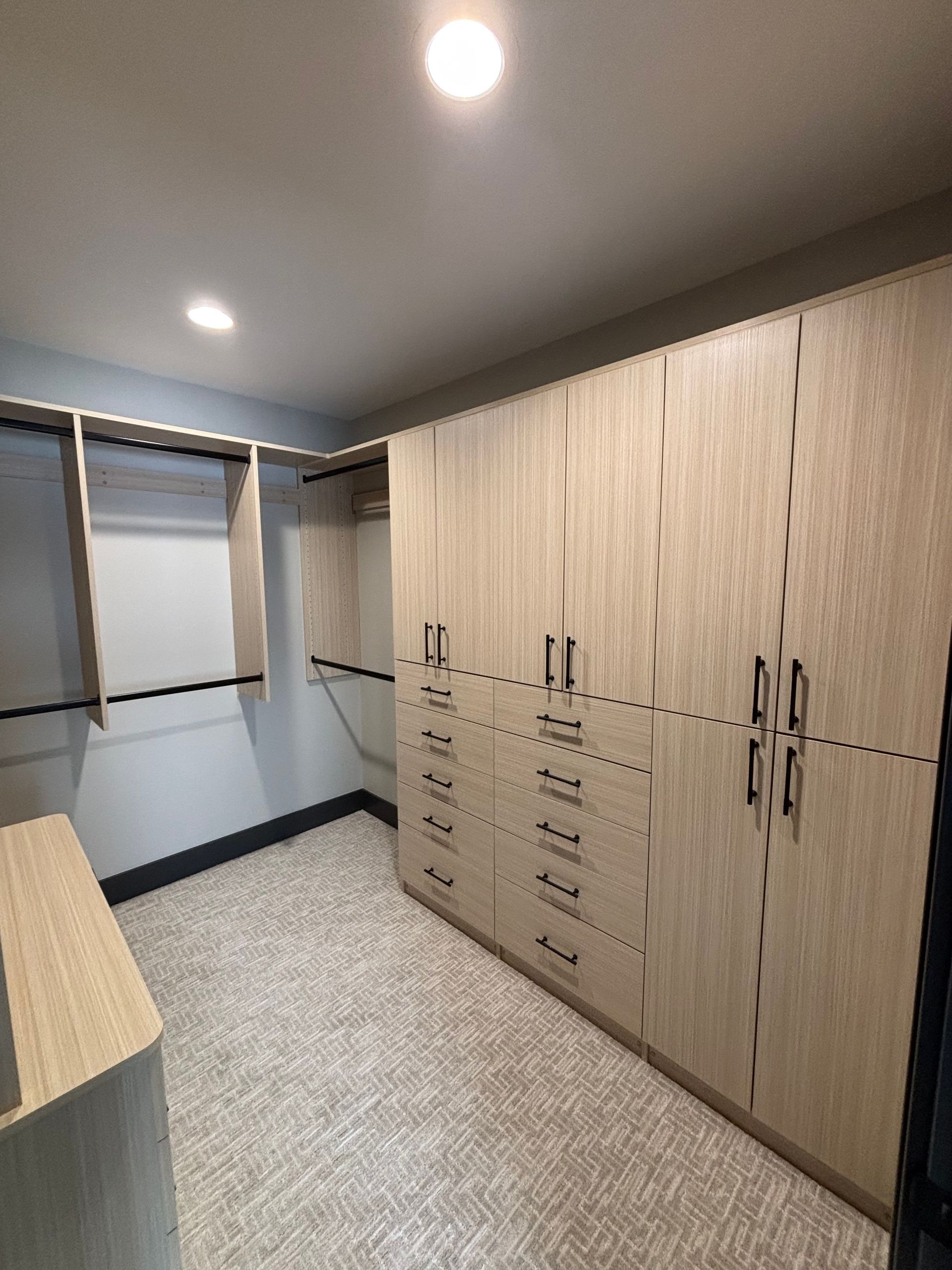 Walk-in closet with wood cabinets, hanging rods, and mirrored doors under ceiling lights.