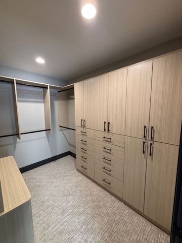 Modern walk-in closet with light wood cabinets, open hanging space, mirrors, and carpeted floor