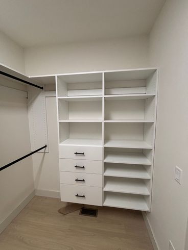 White walk-in closet with shelves, drawers, hanging rods, and beige carpet.