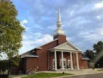 Brick church with white columns, steeple, and cloudy sky.