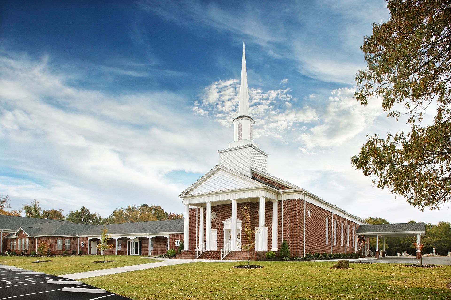 Brick church building with white columns and steeple under a blue sky.