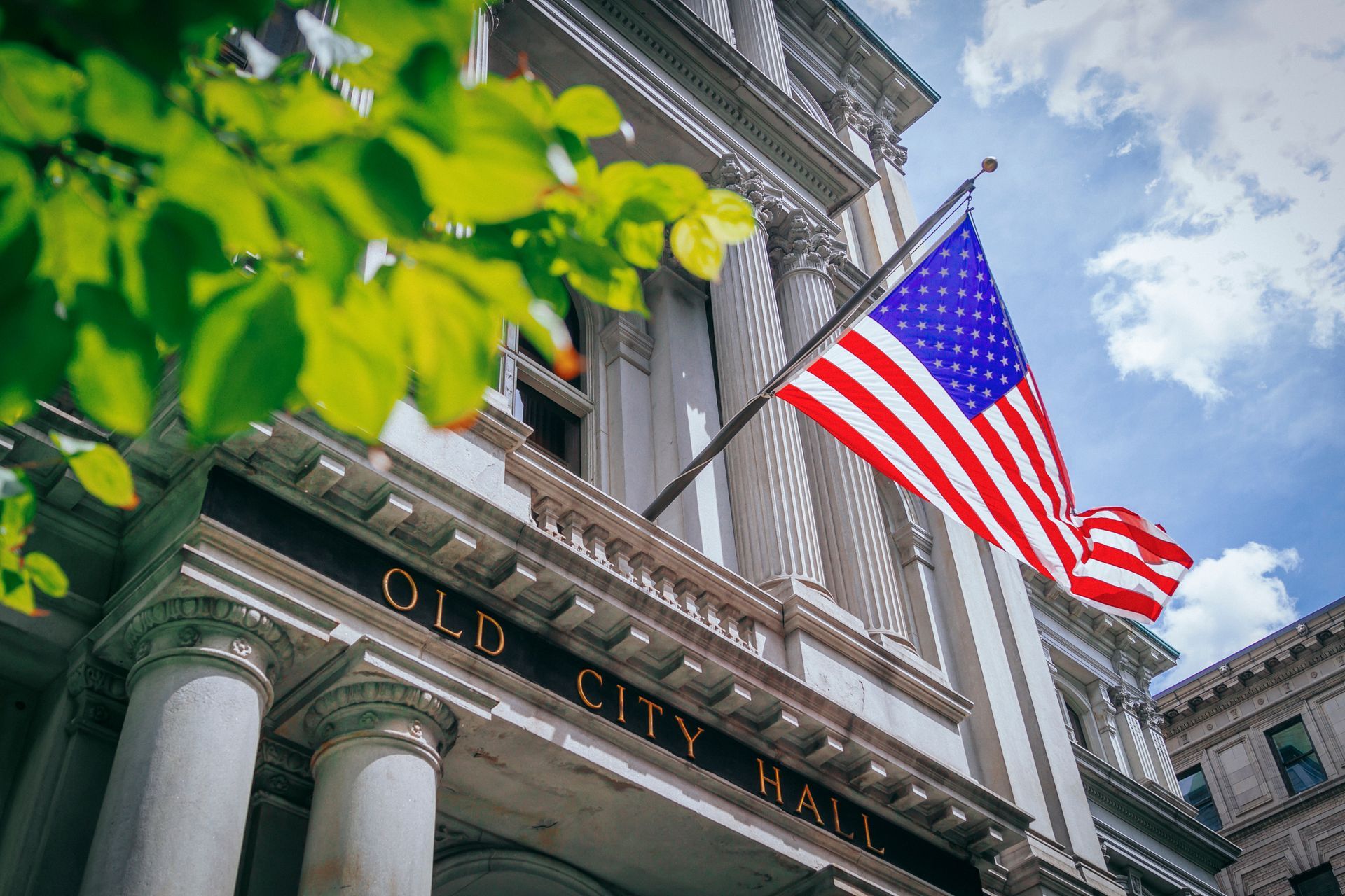 Old City Hall with American flag waving against a partly cloudy sky.