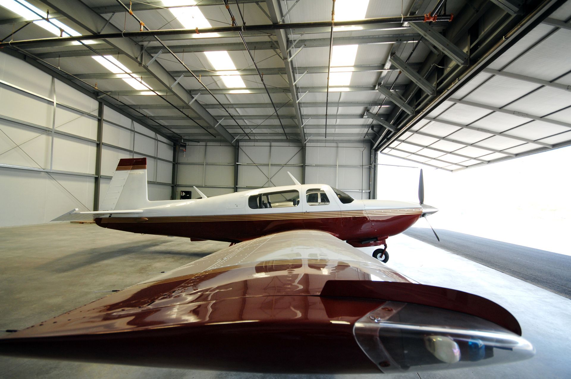 Airplane wing in foreground, another airplane inside a hangar. Hangar has bright overhead lights.