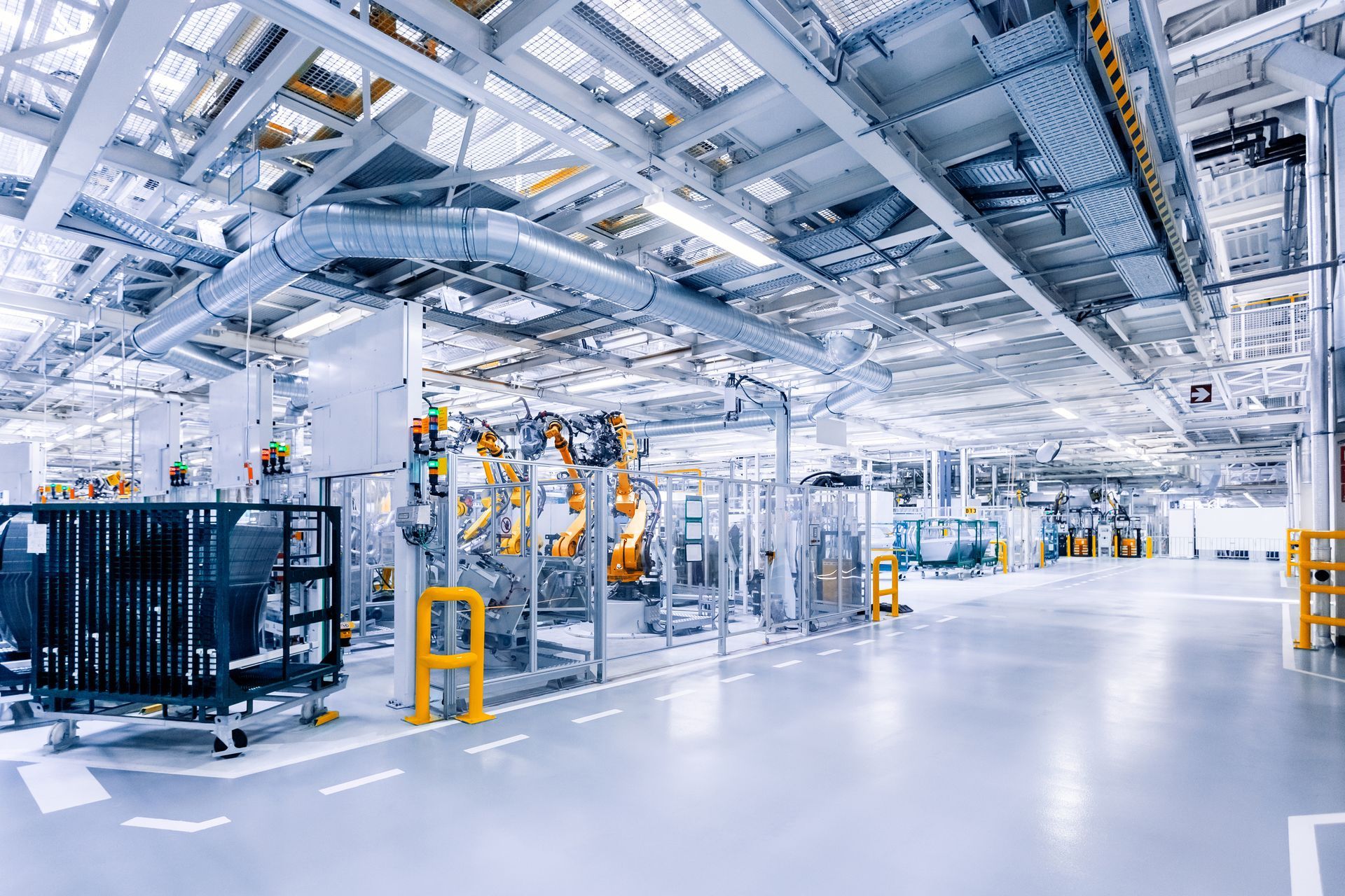 Bright factory interior with machinery, robots, and various equipment under a high ceiling.