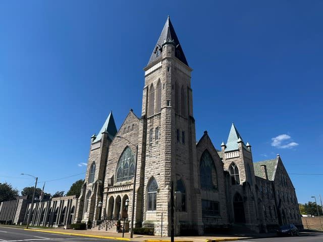 Stone church with a tall steeple against a blue sky.