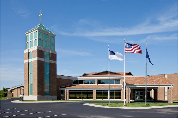 Brick church with a tall steeple, flags flying, and a blue sky.