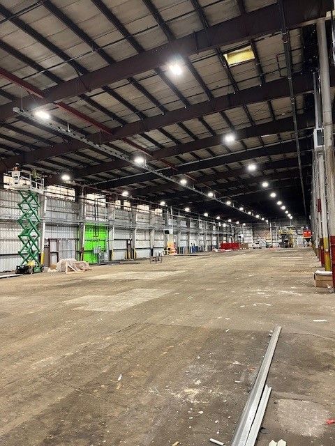 Large empty warehouse with high ceiling, metal beams, and bright overhead lights.