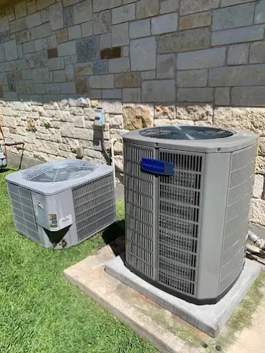 Two air conditioners are sitting on top of a concrete platform in front of a brick wall.