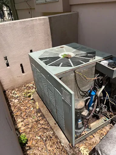 A broken air conditioner is sitting on the ground next to a wall.